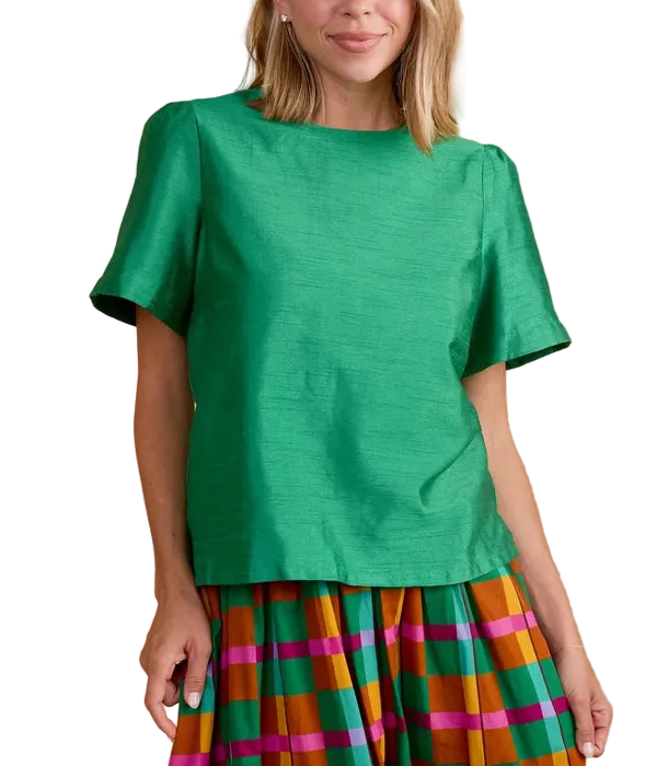 A woman modeling a bright green short-sleeve top with a textured fabric, paired with a colorful striped skirt, against a solid tan background.