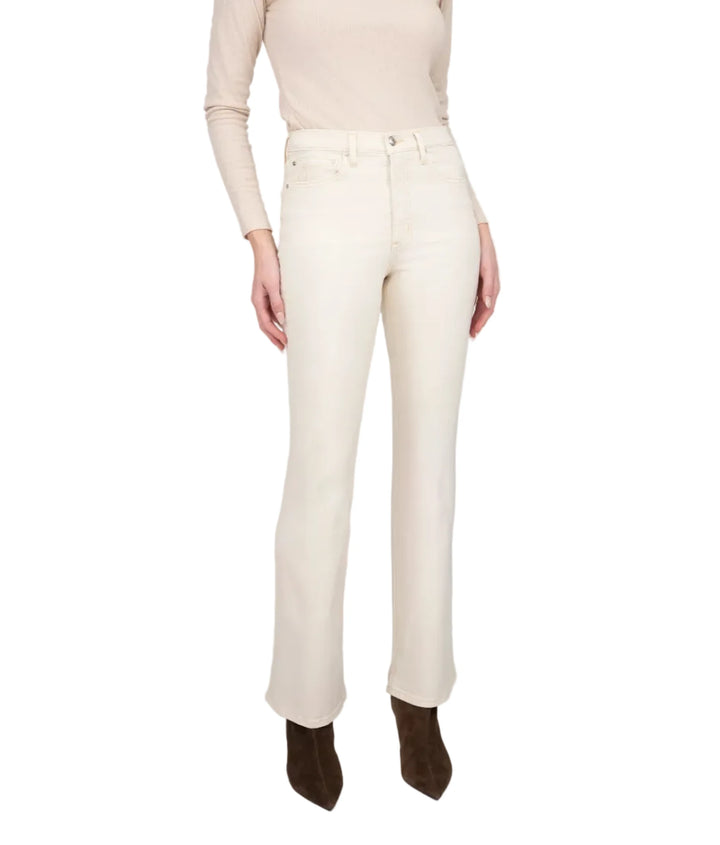 A woman modeling a cream long-sleeve knit top and matching cream straight-leg jeans with dark brown pointed-toe ankle boots, standing against a light gray studio background.