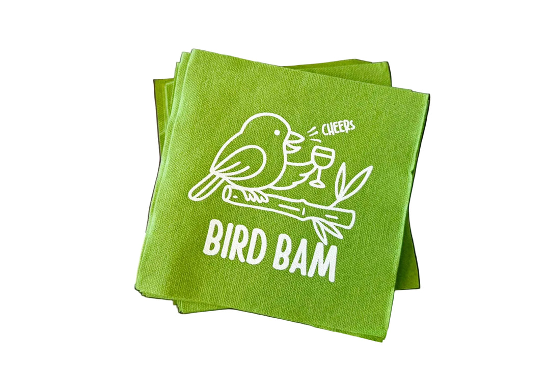 Green napkin with 'Bird Bam' design surrounded by white tiles on a purple background