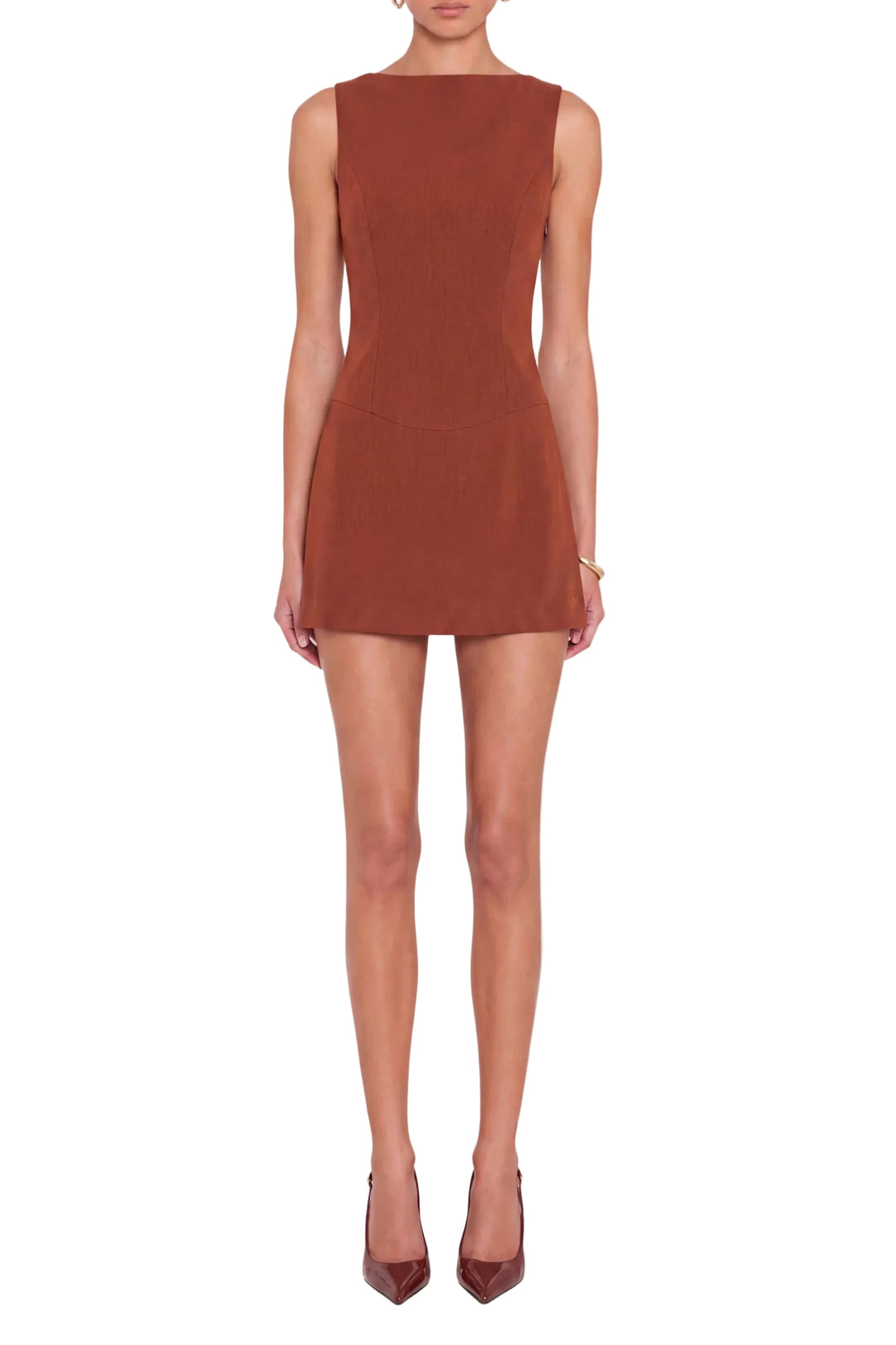 A woman modeling a sleeveless, bodycon mini dress in a warm rust or terracotta color, paired with matching pointed-toe heels, against a solid light gray background.