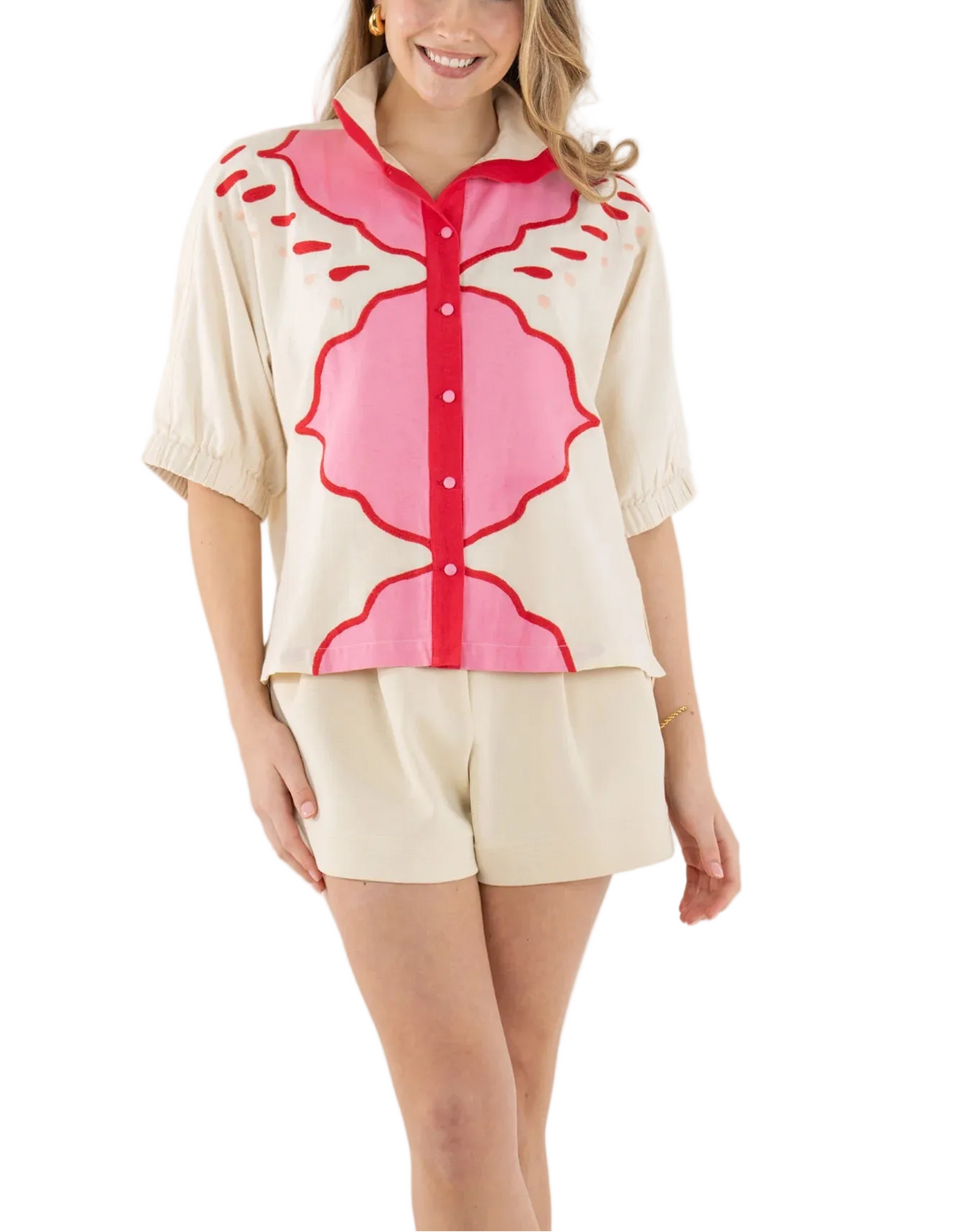 The Bonny Top in Pink Palace draws inspiration from the ornate geometric designs and romantic hues of Jaipur’s storied architecture. Intricate embroidery adds dimension and artistry, creating a striking interplay of pattern and texture. Designed with a classic stand collar, covered front button closure, and relaxed dolman sleeves with soft elastic cuffs, the silhouette drapes with effortless ease. 