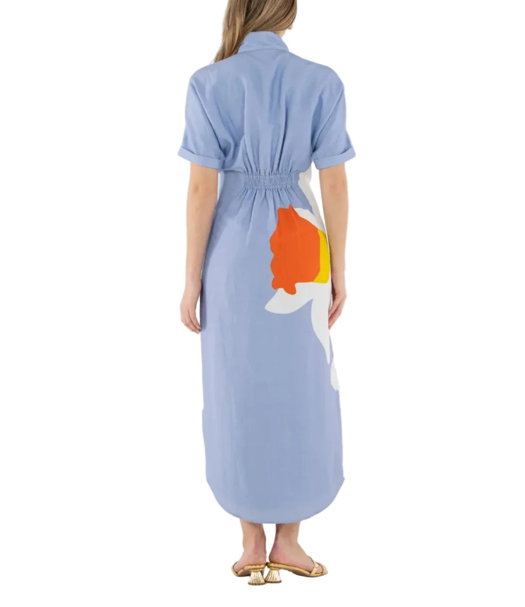 Woman wearing a light blue dress with a colorful design on the back, standing against a white background.