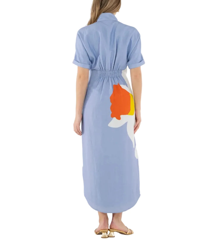 Woman wearing a light blue dress with a colorful design on the back, standing against a white background.