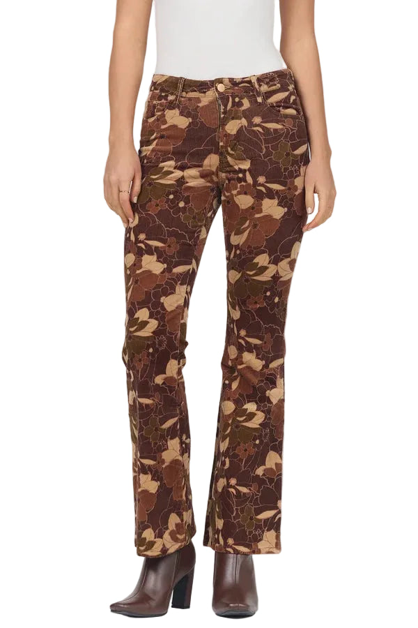 A model wearing a pair of brown camouflage pants with a white top and dark brown heeled ankle boots, shown from the waist down against a light gray studio background.