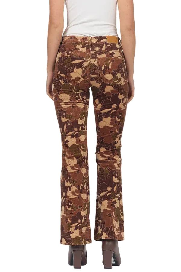 A person shown from the back wearing brown camouflage flared pants, a white top, and dark brown heeled shoes against a light gray studio background.