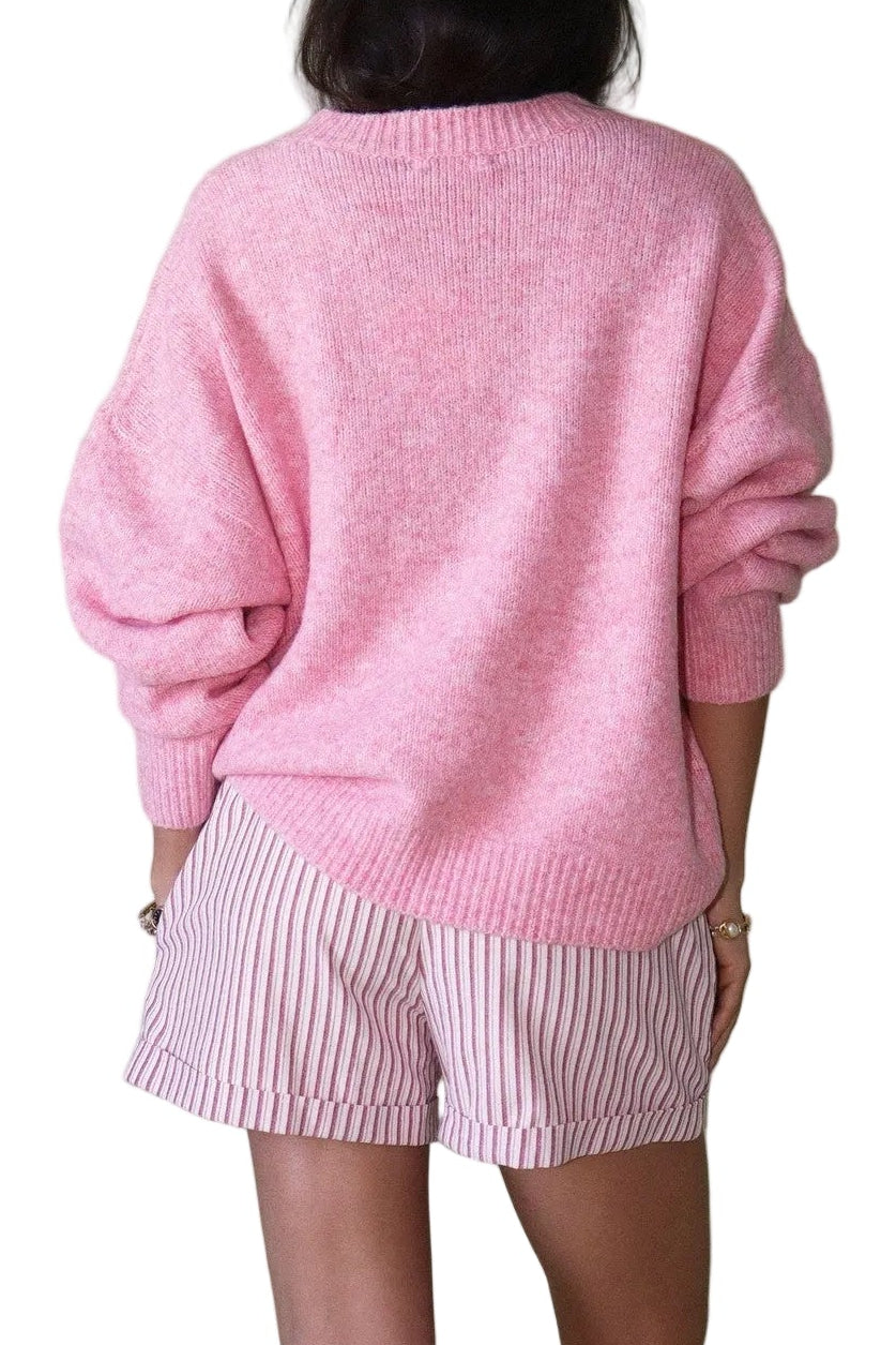 Person wearing a pink sweater and shorts with a cap on a plain background