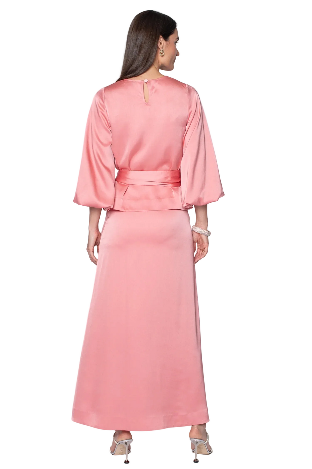 A woman shown from the back wearing a long, flowing pink satin dress with three-quarter sleeves and a matching waist tie, photographed against a plain light gray studio background.