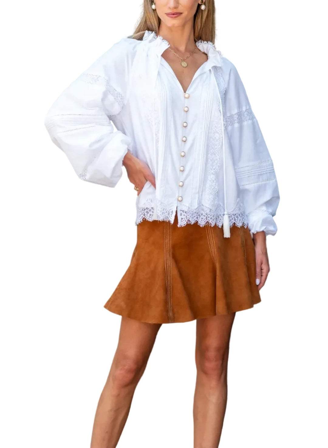 A woman stands outdoors in front of a blue door and brick wall, wearing a loose white long-sleeve blouse with lace trim and a brown mini skirt, paired with brown ankle boots.