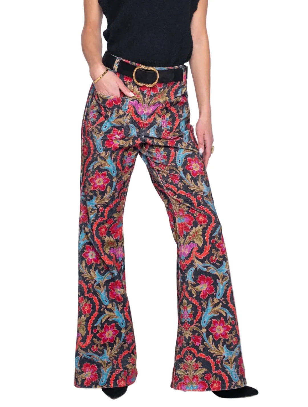 A woman modeling high-waisted, wide-leg pants with a vibrant red, blue, and green paisley pattern, styled with a black sleeveless turtleneck top and a black belt with a gold buckle.