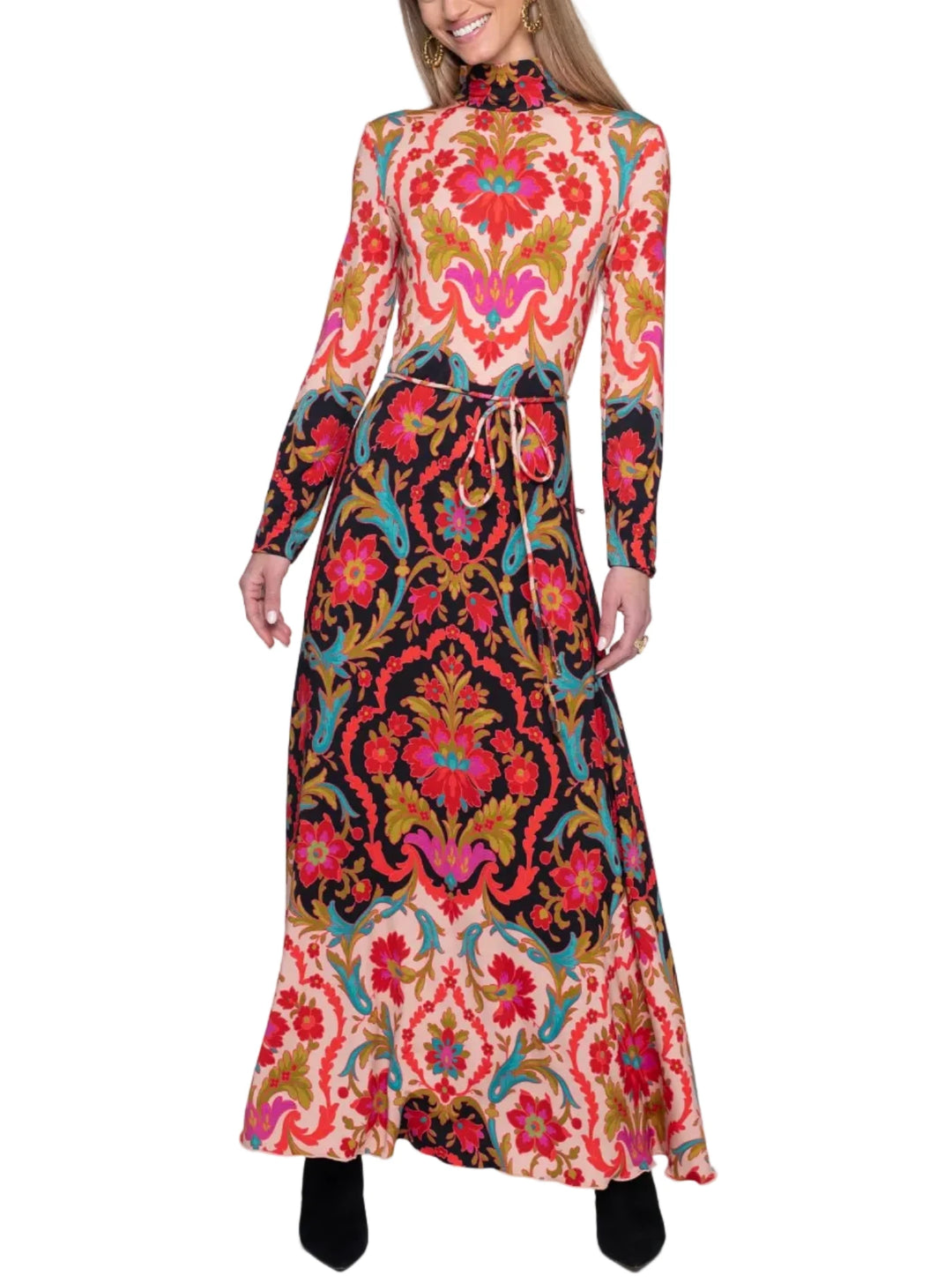 A woman modeling a long-sleeved high-neck maxi dress with an intricate, colorful baroque-style floral pattern in red, pink, blue, gold, and black, paired with black pointed-toe heels against a plain white studio background.