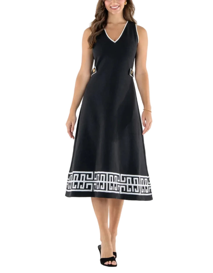 A woman modeling a sleeveless black midi dress with a V-neckline, side pockets, and a white Greek key pattern border at the hem, set against a plain white studio background.