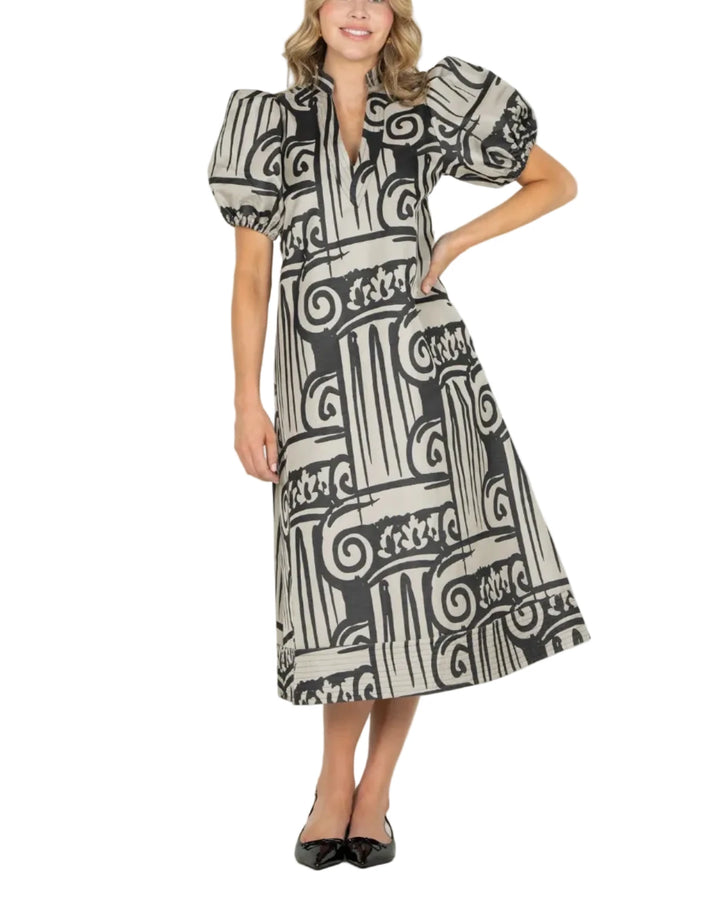 A woman modeling a black and white geometric print midi dress with puff sleeves and a V-neckline, standing against a plain white studio background.