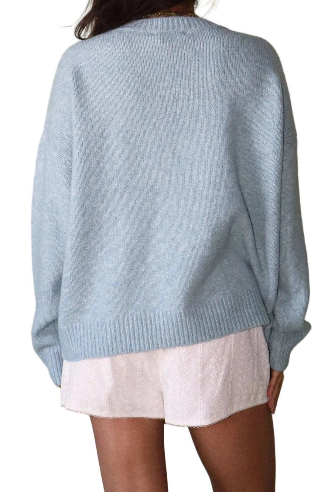 Person wearing a light blue sweater and white shorts against a plain background