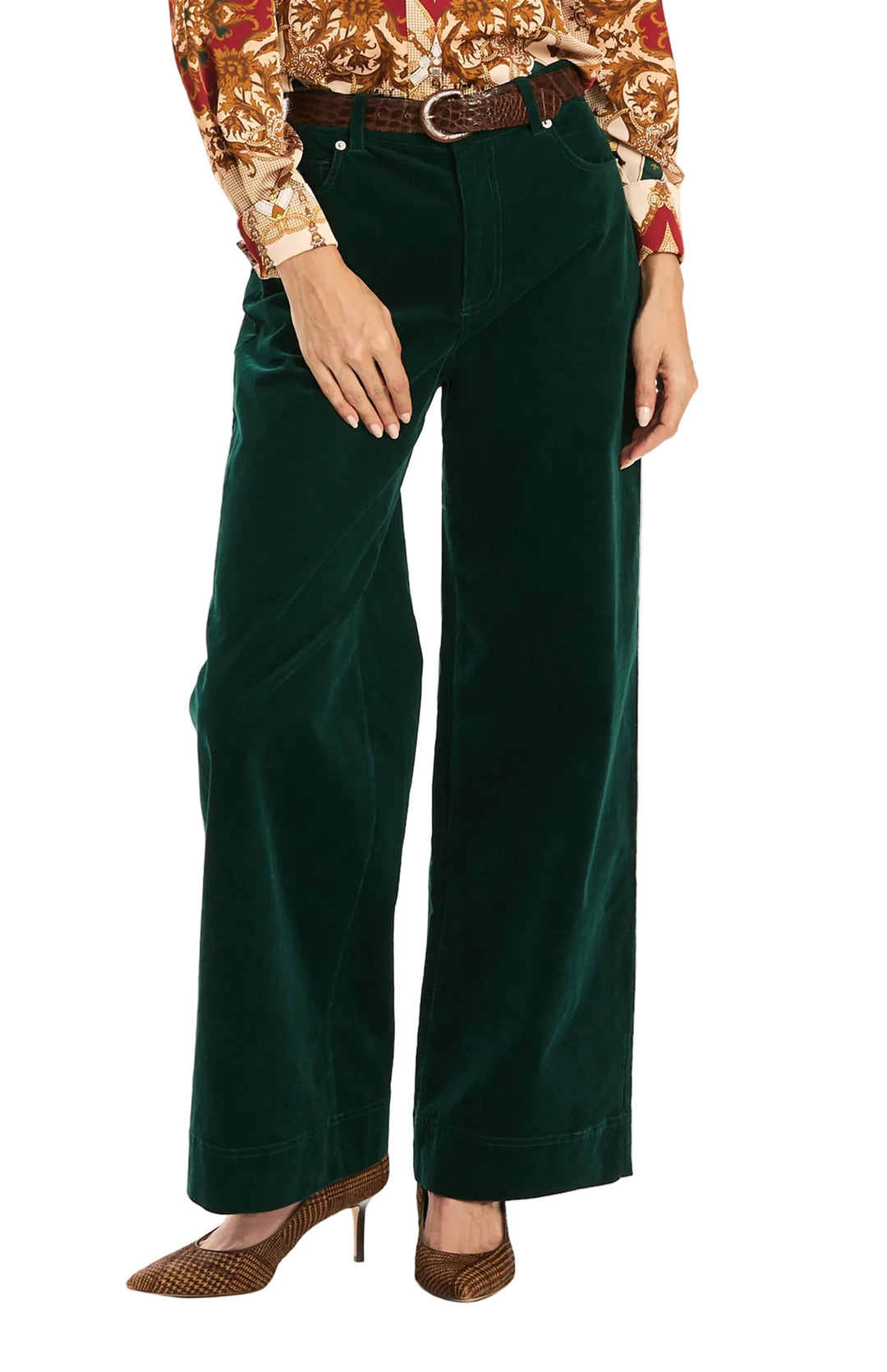 A model wearing dark green velvet wide-leg trousers, styled with a brown belt, a patterned long-sleeve top, and brown pointed-toe heels against a plain white studio background.