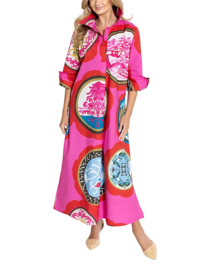 A woman modeling a vibrant pink maxi dress with a bold multicolor circular and botanical print, standing against a plain white studio background.