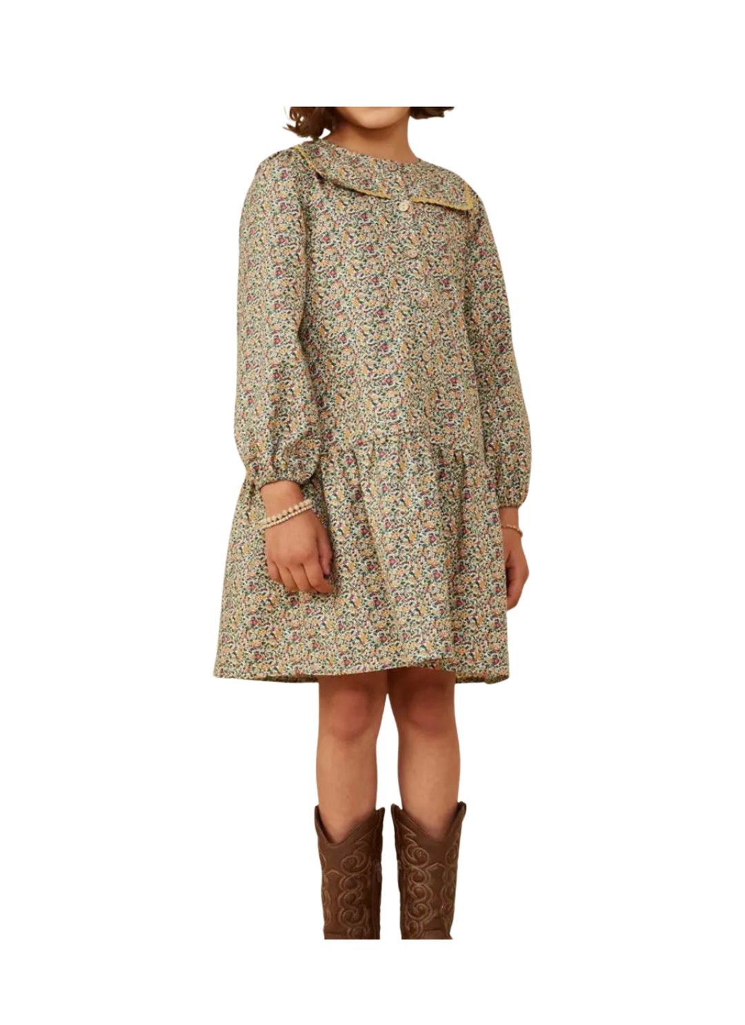 A child wearing a long-sleeve, knee-length dress with a dense multicolor floral and paisley print on a light beige base, paired with brown cowboy boots, shown against a plain white background.