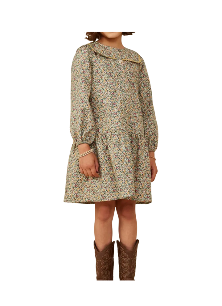 A child wearing a long-sleeve, knee-length dress with a dense multicolor floral and paisley print on a light beige base, paired with brown cowboy boots, shown against a plain white background.