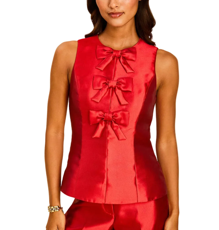 A woman modeling a sleeveless red satin vest with three large bow details down the front, paired with matching red satin pants, against a solid beige background.