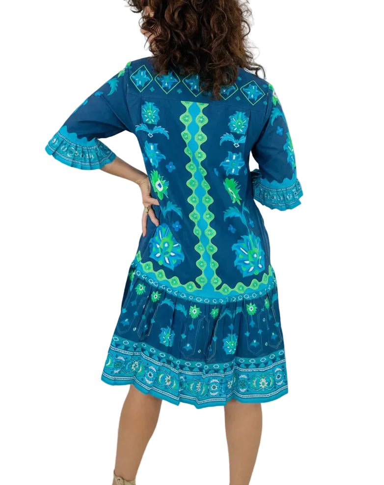 Woman wearing a blue dress with green patterns against a gray background