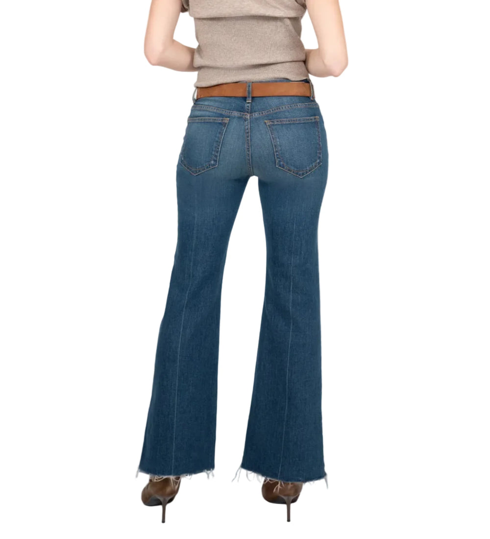 A woman is shown from behind wearing blue flare jeans, a beige sleeveless top, and brown heels against a light gray studio background.