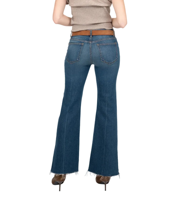 A woman is shown from behind wearing blue flare jeans, a beige sleeveless top, and brown heels against a light gray studio background.