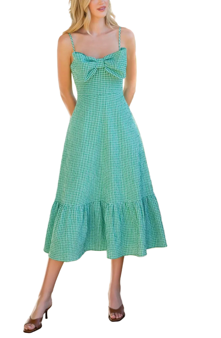 Woman in a green checkered dress standing outdoors with plants and a stone path in the background