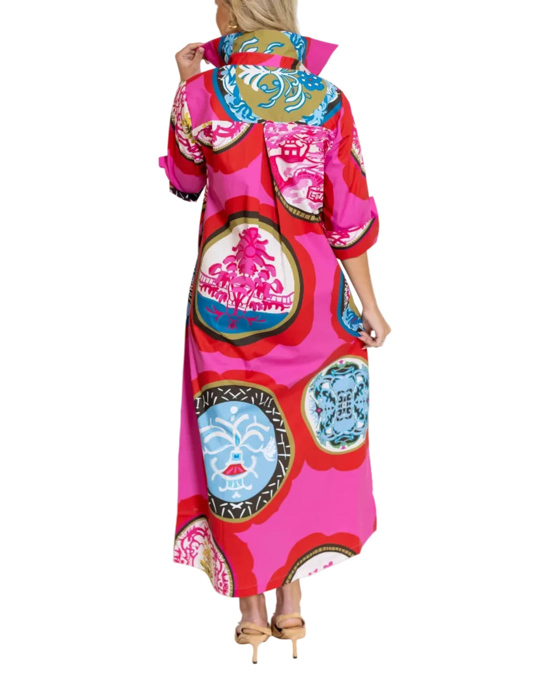 A woman viewed from behind wearing a vibrant pink maxi dress with a bold multicolor abstract print, paired with beige high-heeled sandals, against a plain white studio background.