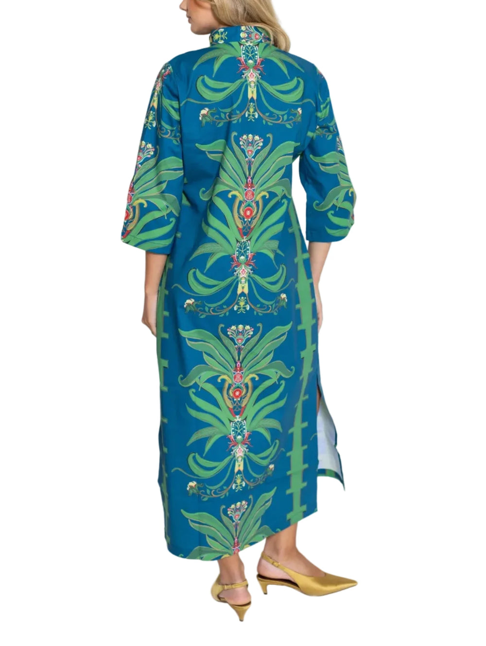A woman shown from the back wearing a long teal blue maxi dress with a green and multicolor floral pattern, paired with gold pointed-toe flats, against a light gray studio background.