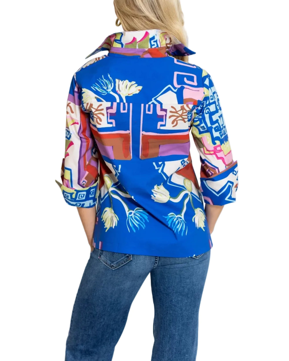 A woman viewed from behind wearing a vibrant blue button-up shirt with a multicolor abstract and floral pattern, paired with blue jeans, against a plain white background.