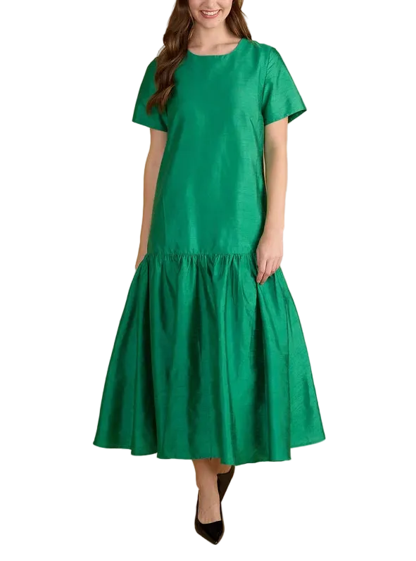A woman modeling a bright green midi dress with short sleeves and a tiered skirt, standing against a solid beige studio background.