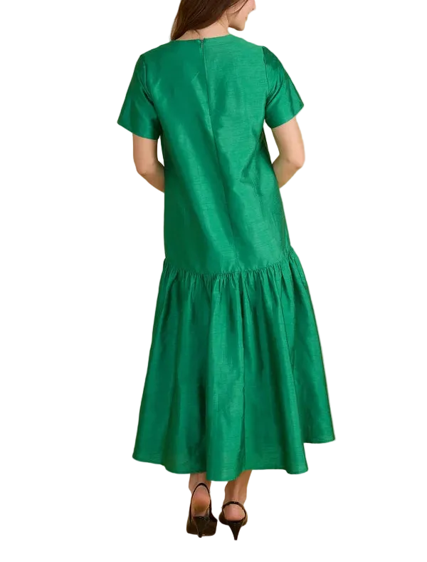 A woman viewed from the back wearing a bright green short-sleeve midi dress with a tiered skirt, standing against a solid beige studio background.