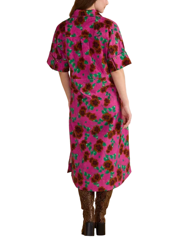 A woman viewed from the back wearing a short-sleeve pink dress with a dark floral print and green accents, paired with brown patterned boots, against a solid beige studio background.