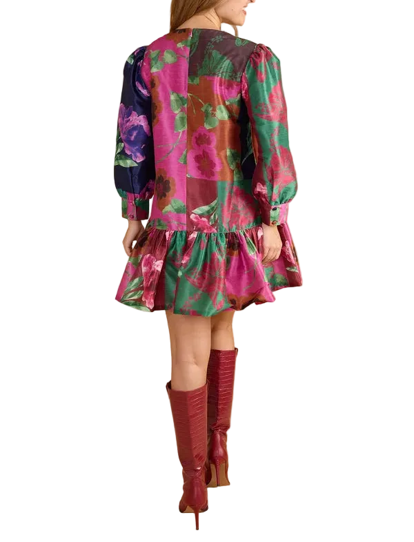 A woman shown from the back wearing a short floral print dress with long puff sleeves and a ruffled hem, paired with knee-high burgundy boots, against a solid beige studio background.