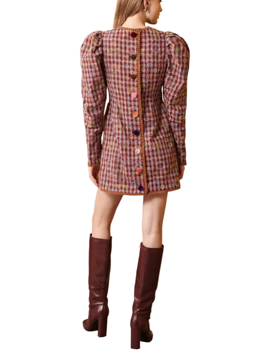 Woman wearing a plaid dress and brown knee-high boots standing in a room with a yellow wall and brown chair.
