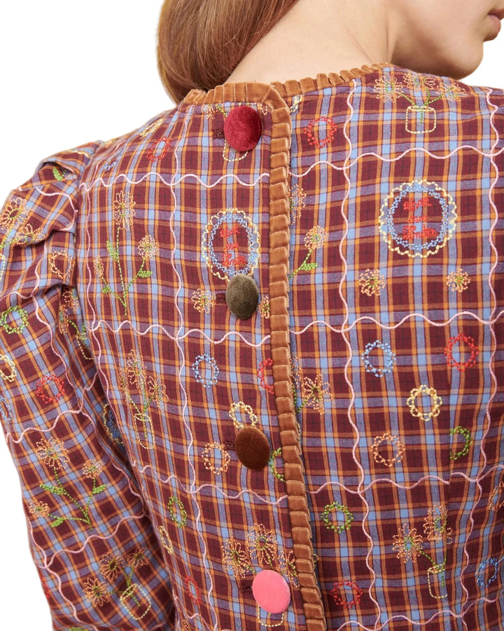 Close-up of the back of a vintage-style dress or jacket featuring a brown and blue plaid pattern, embroidered floral motifs, a brown velvet trim along the back opening, and decorative buttons.