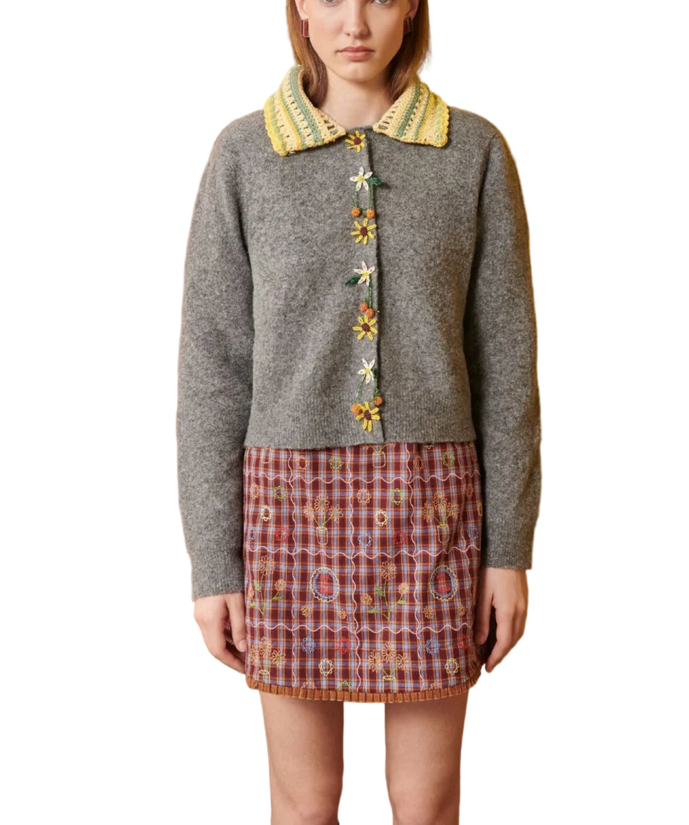 Woman wearing a gray cardigan with floral buttons against a yellow wall.