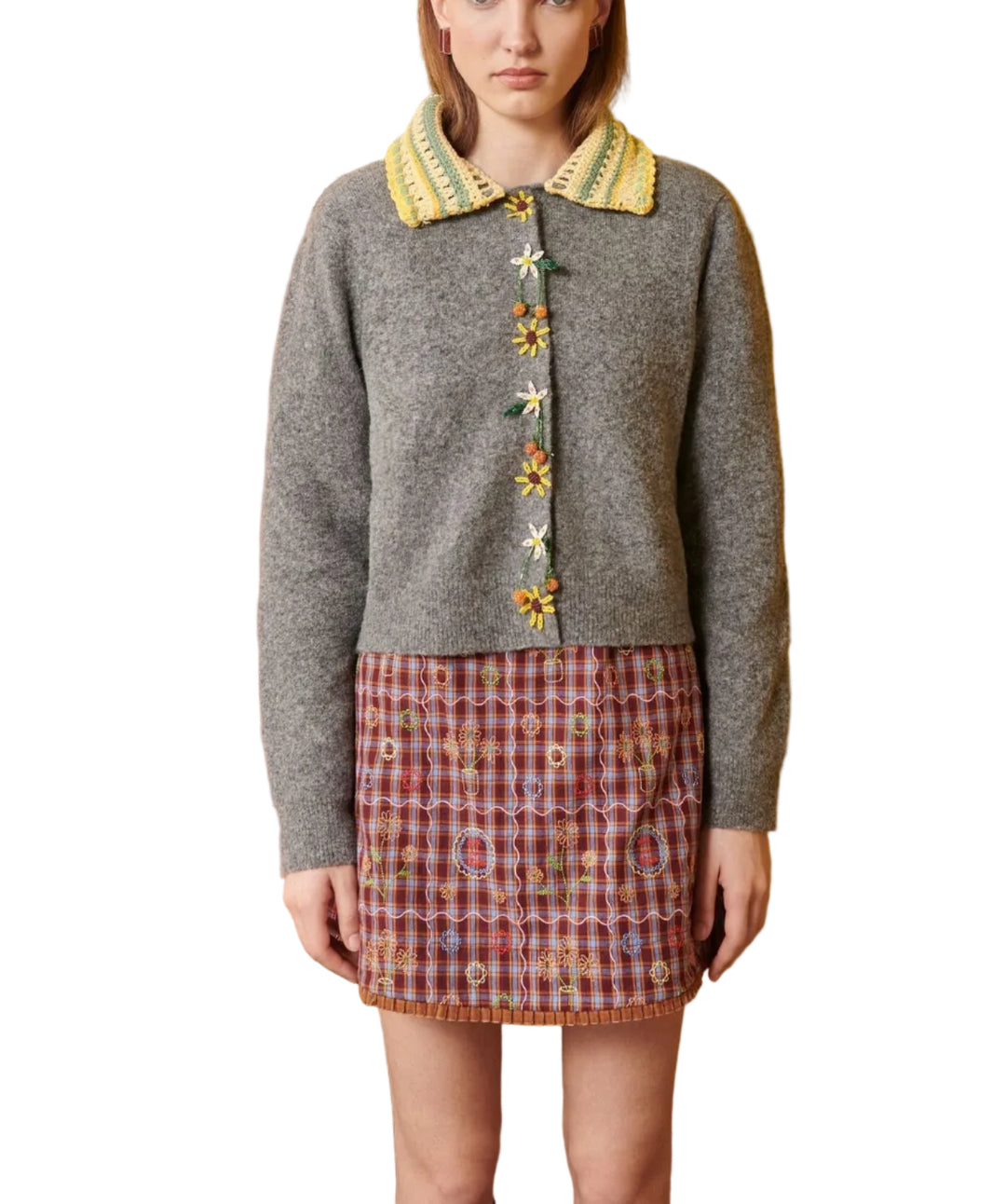 Woman wearing a gray cardigan with floral buttons against a yellow wall.