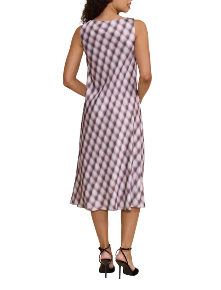 A woman shown from the back wearing a sleeveless midi dress with a purple and white diagonal diamond pattern, paired with black high heels, against a solid beige studio background.