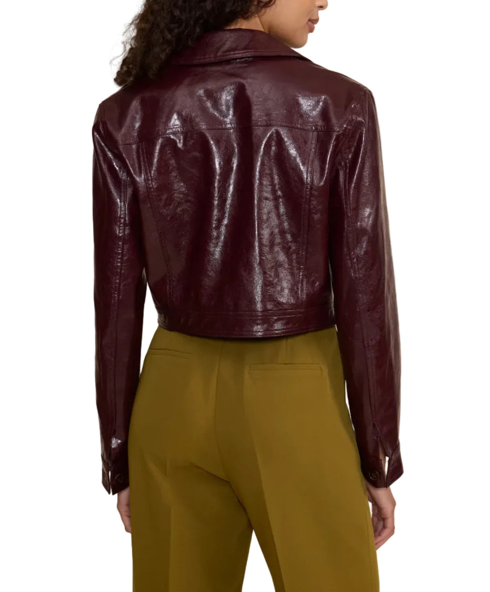 A woman shown from the back wearing a cropped, glossy burgundy faux-leather jacket and olive green trousers, set against a plain beige studio background.