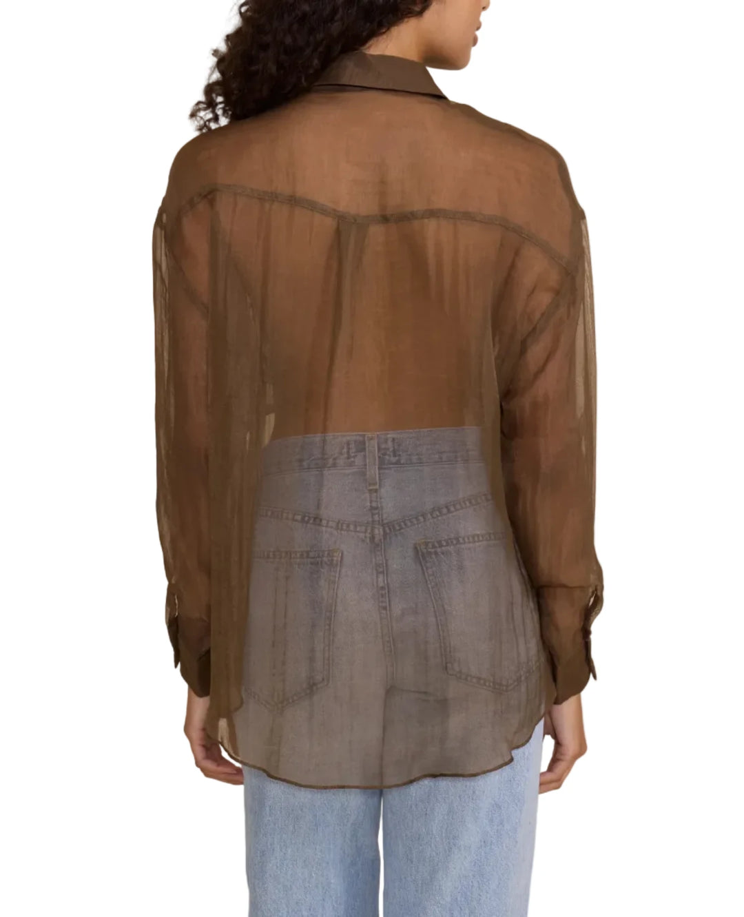 A woman shown from the back wearing a sheer brown button-up shirt over a gray denim skirt, paired with light blue jeans, against a solid beige background.