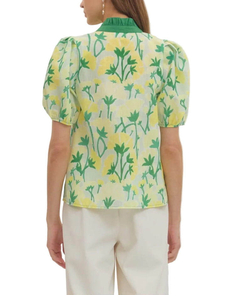 Woman wearing a floral blouse with green and yellow flowers on a plain background