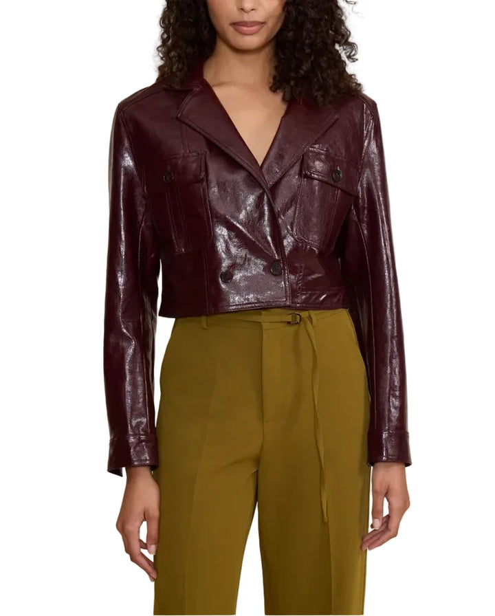 A woman modeling a cropped, glossy burgundy faux-leather jacket with a wrap-style front, paired with olive green trousers, against a solid beige background.