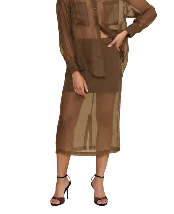 A model wearing a sheer brown button-up shirt and matching midi skirt set, styled with black strappy heels against a solid beige studio background.