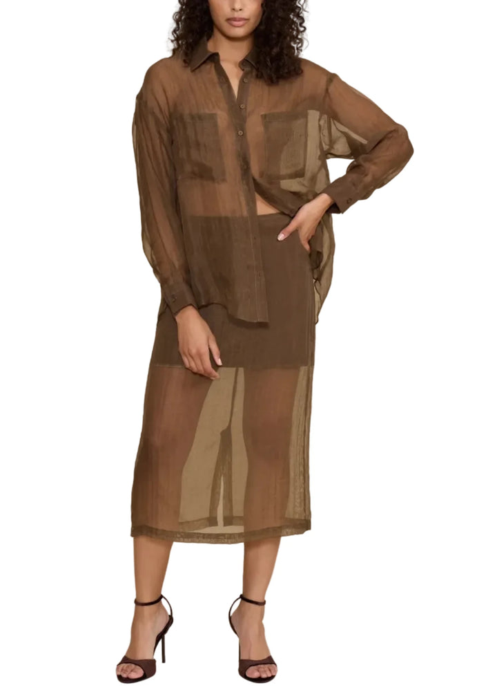 A model wearing a sheer brown button-up shirt and matching midi skirt set, styled with black strappy heels against a solid beige studio background.