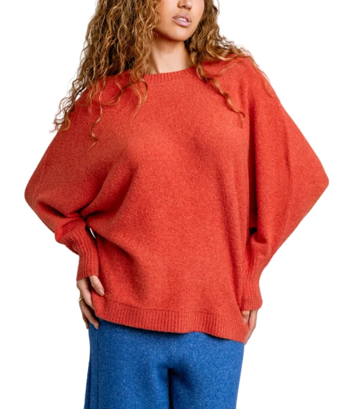 Woman wearing a red sweater and blue pants against a plain background