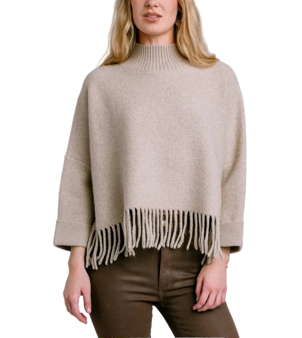 Woman wearing a beige poncho with fringe details against a light gray background