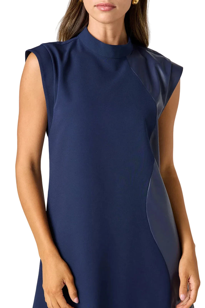A woman wearing a sleeveless navy blue mock-neck dress with sheer side panels, shown from the chin down against a light gray studio background.