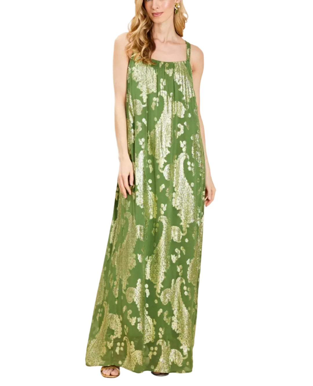 A woman modeling a sleeveless, floor-length green maxi dress with a metallic gold abstract pattern, set against a solid beige studio background.