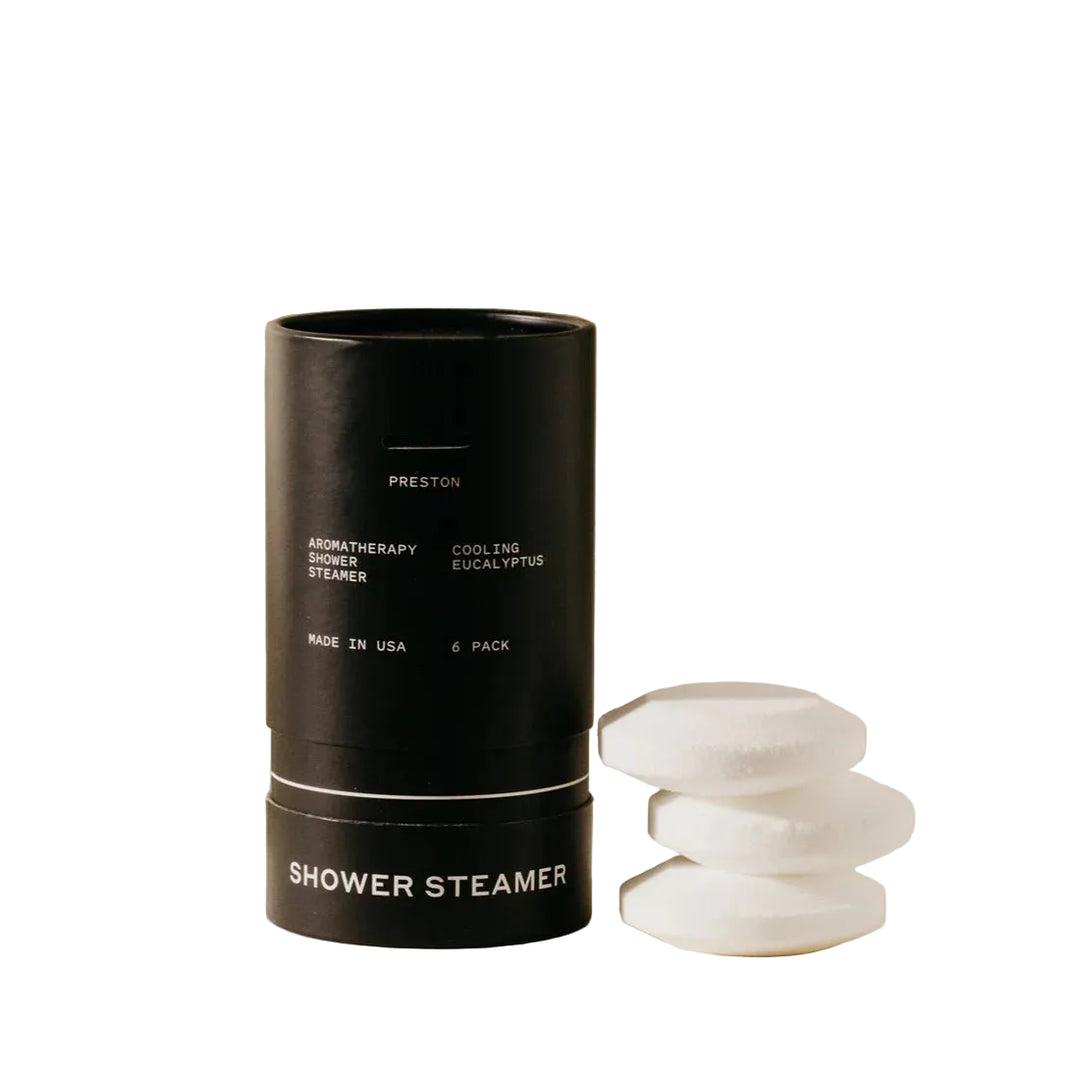 Black cylindrical shower steamer container with white stones on a beige background