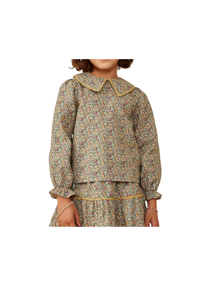 A child wearing a long-sleeve floral print top with a large Peter Pan collar and gold trim, paired with a matching skirt, shown against a plain white background.